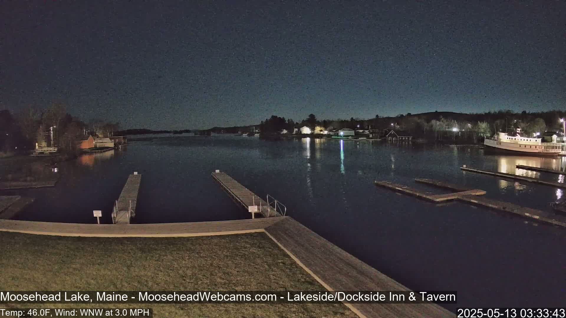 A nighttime view of a calm lake with several docks and buildings along the shore, under a dark sky.