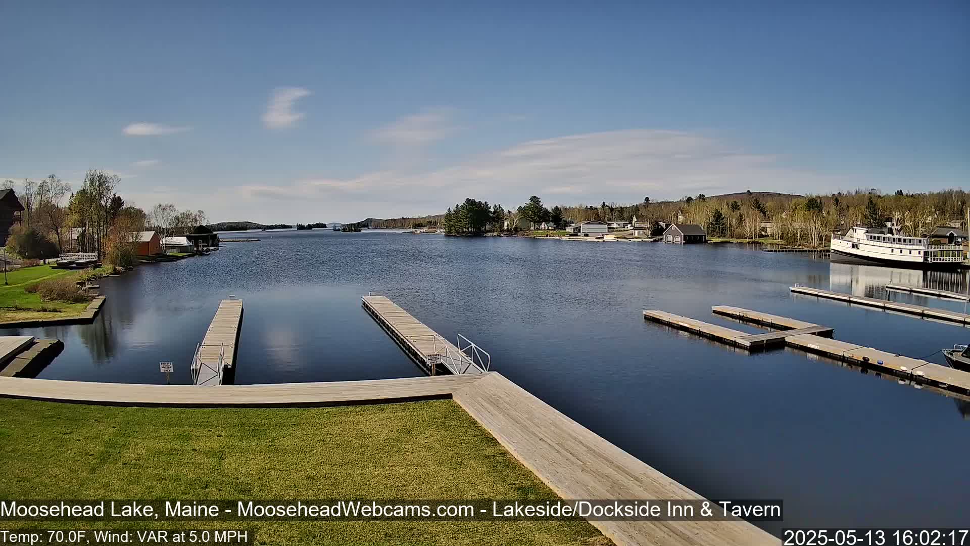 A calm lake with several docks, a boat, and shoreline buildings under a mostly clear, sunny sky.