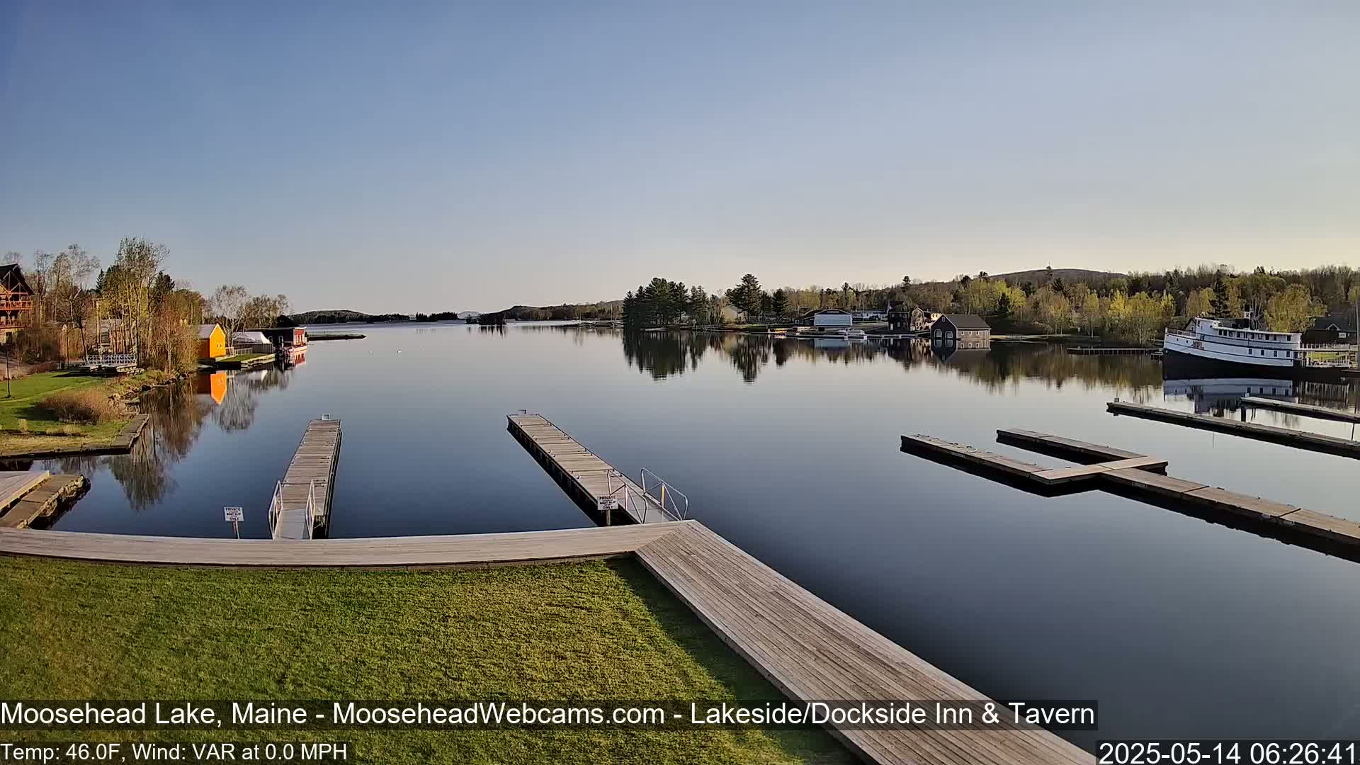 A calm lake with several docks and a large boat is seen from a grassy shoreline on a clear day.