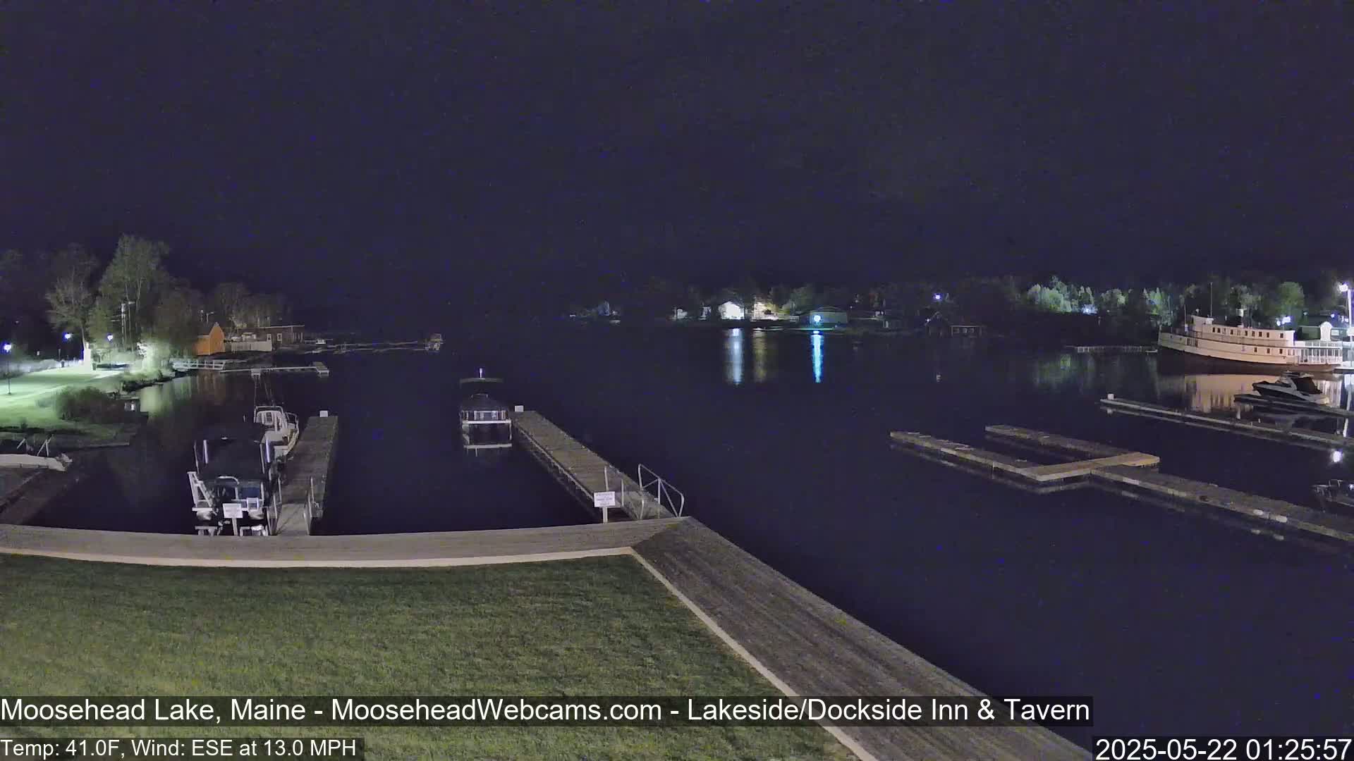 A nighttime view of a calm lake with boats docked at piers, under a dark sky.