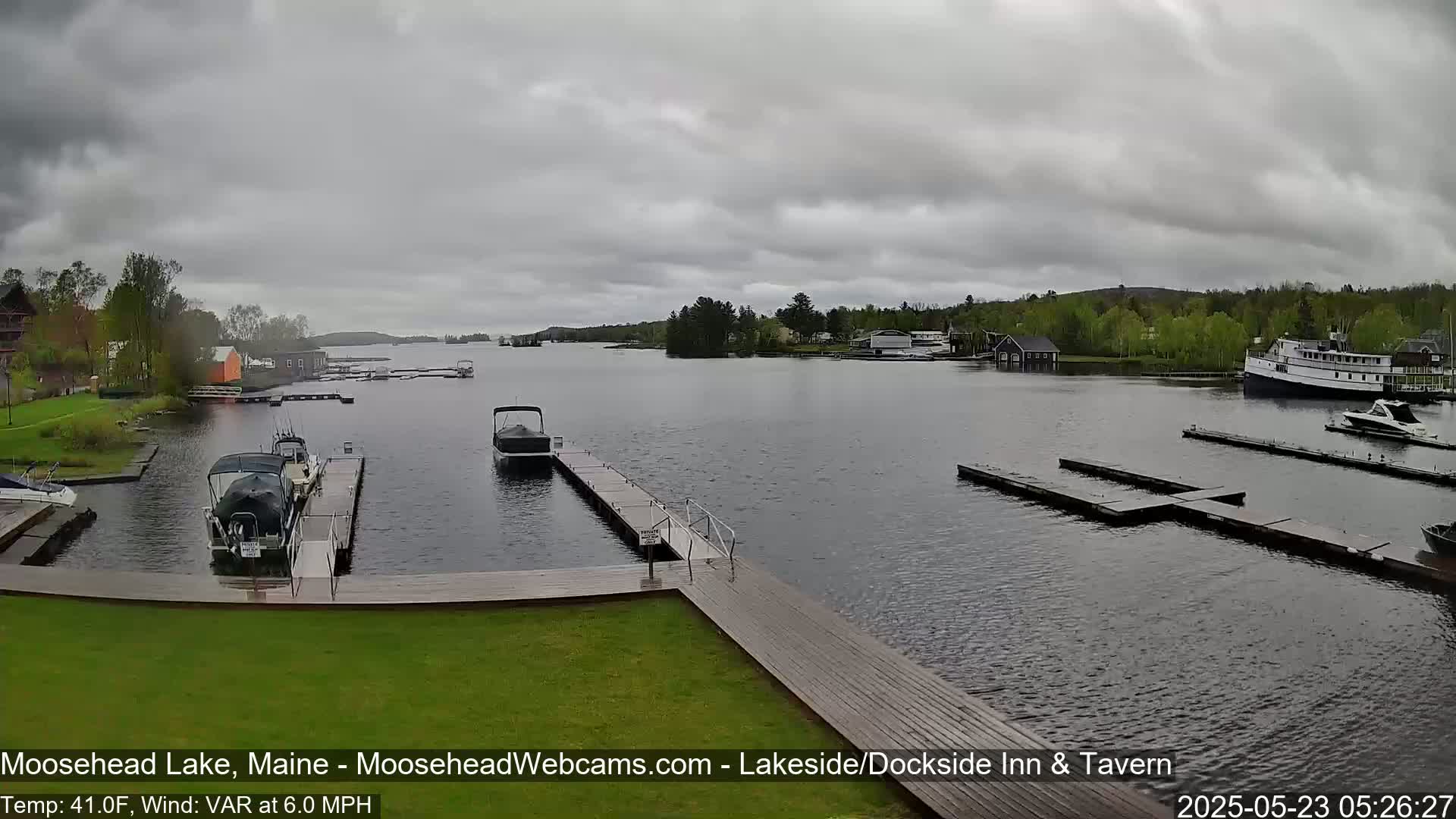 Several boats are moored at docks on a calm lake under a cloudy sky.
