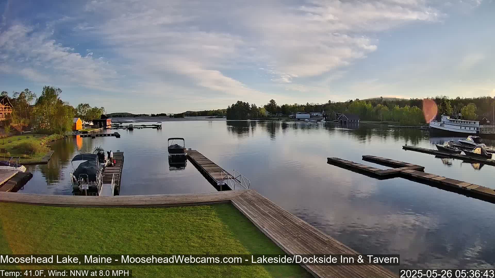 A calm lake with several boats docked at piers, under a partly cloudy sky.