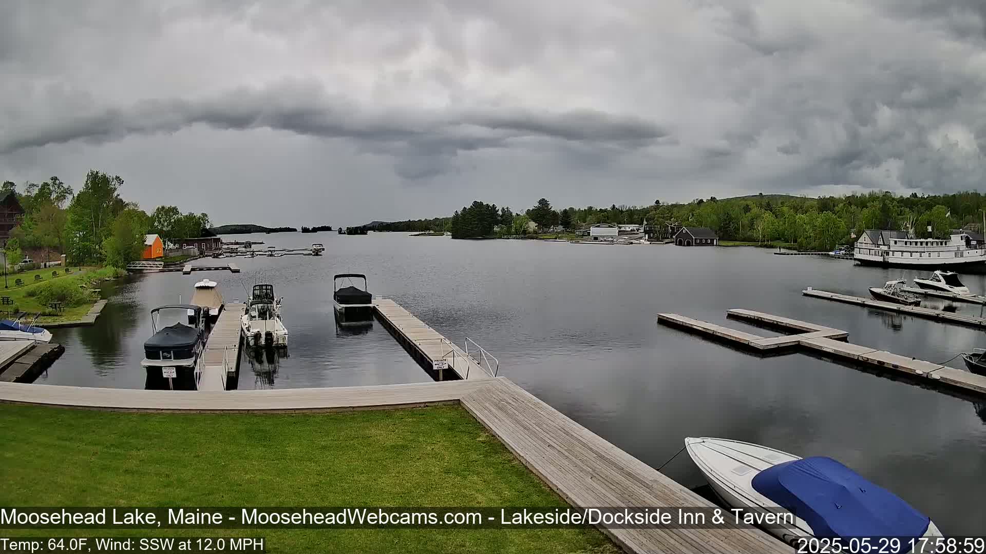 A calm lake with several boats docked at piers under a cloudy sky.