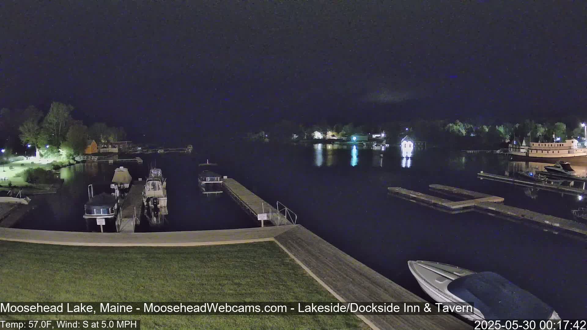 A nighttime view of a calm lake with boats docked at piers under a dark sky.