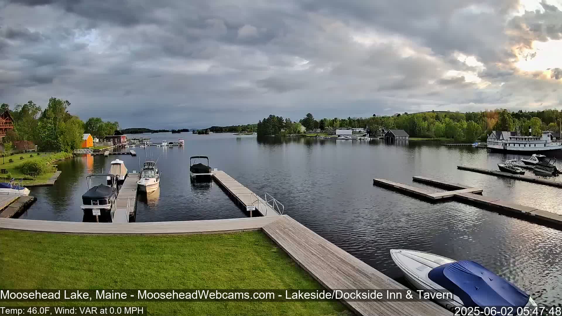 A calm lake with several boats docked at piers, under a partly cloudy sky.