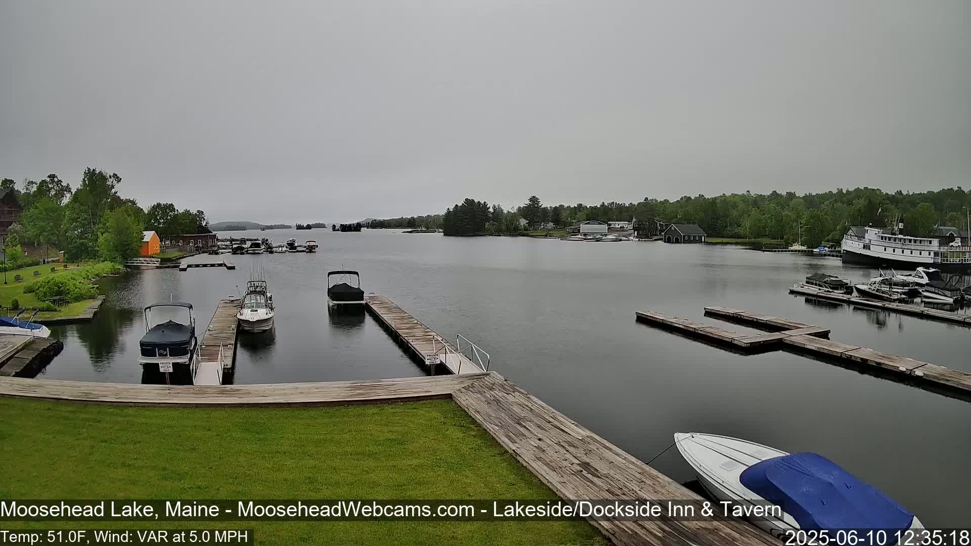 A calm lake with several boats docked at wooden piers under an overcast sky.