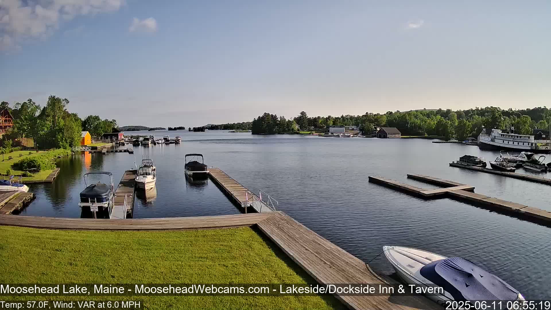 A calm lake with several boats docked at piers, under a mostly clear sky.