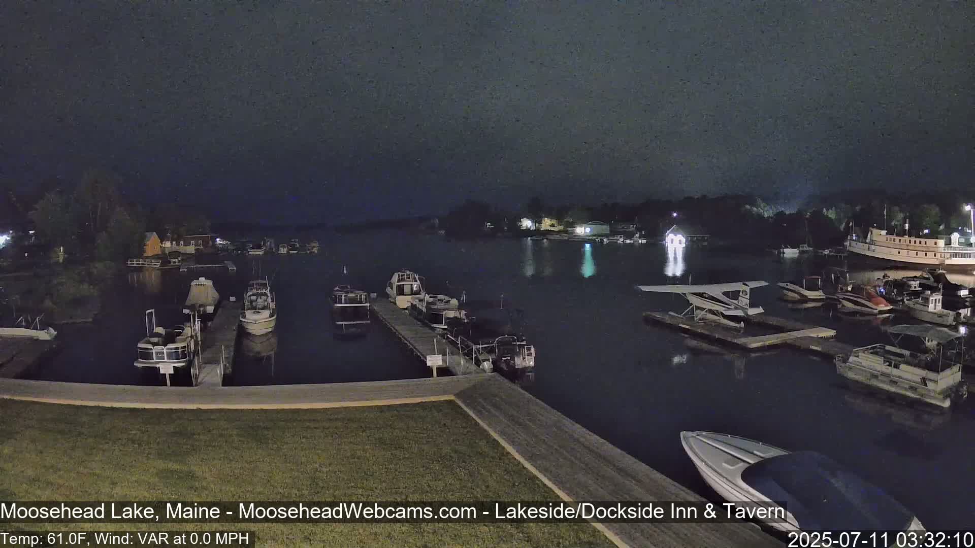 Numerous boats are moored at a dock on a dark, calm lake at night.