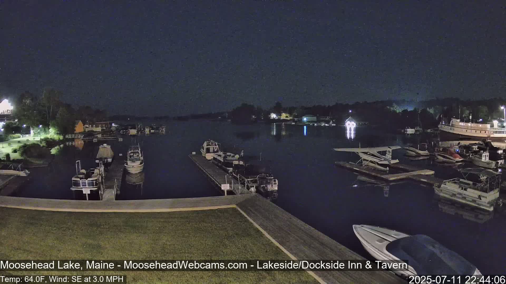 Numerous boats are moored at a dock on a dark, calm lake at night.