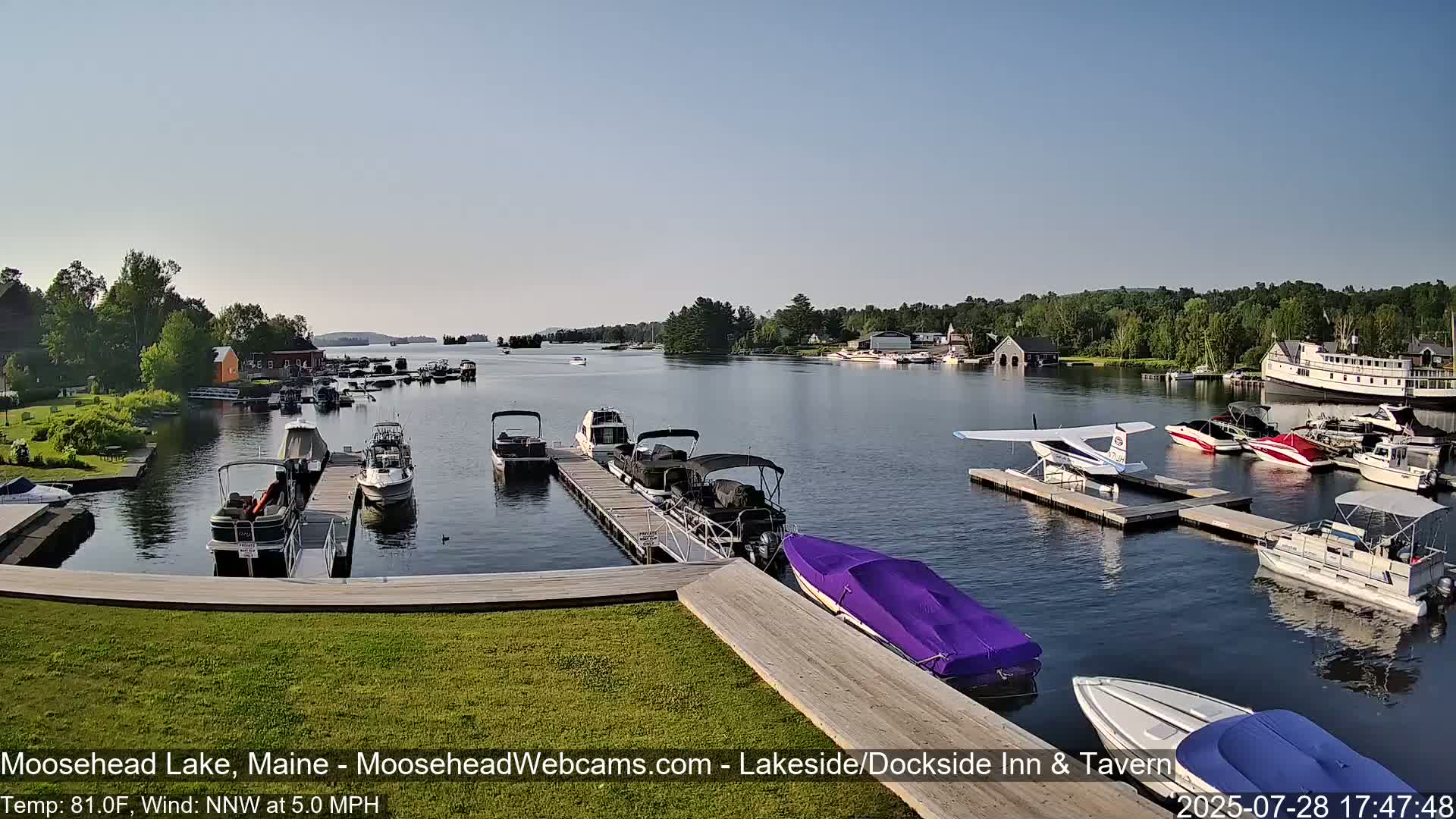 A calm lake with numerous boats docked at piers, under a clear, sunny sky.