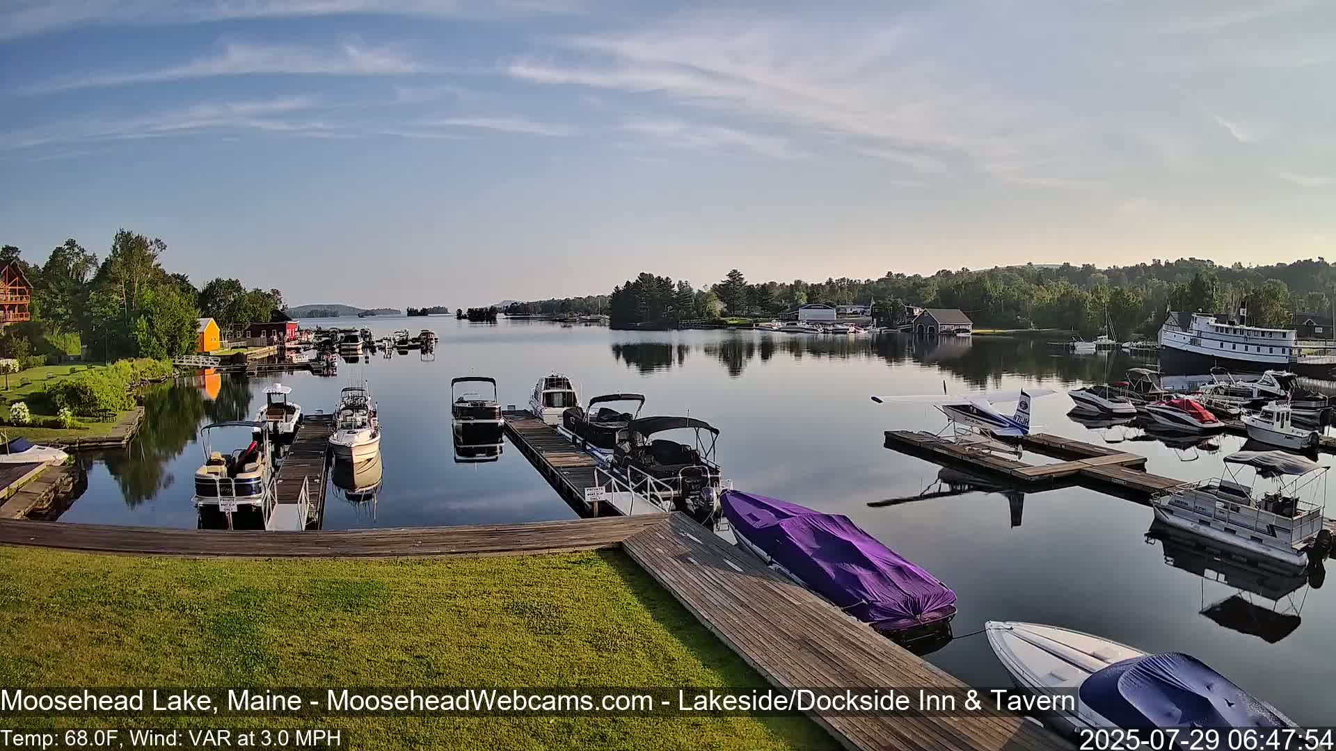 A calm lake with numerous boats docked at piers, under a clear, sunny sky.