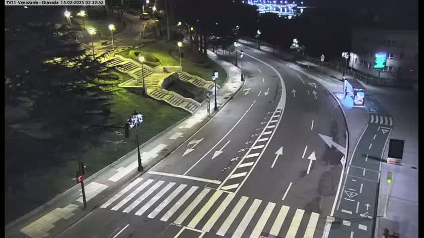 A nighttime, overhead view of a mostly empty roadway curving around a park with stairs, illuminated by streetlights.