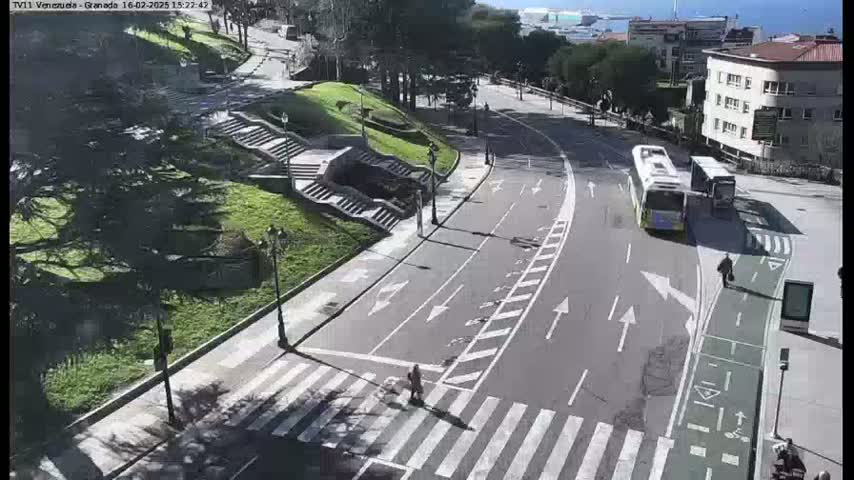 A sunny day overlooking a city street with a bus stop, a pedestrian crossing, and a set of stairs leading down to a park-like area.