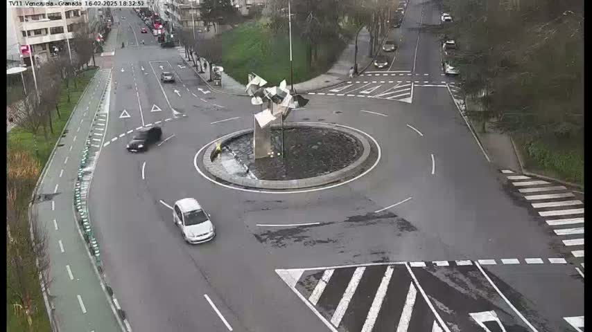 A traffic roundabout with several cars is shown on a gray overcast day.