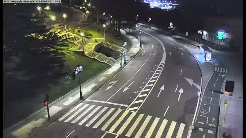 A nighttime street scene shows a curved road with crosswalks, streetlights, and stairs leading down to a park-like area.