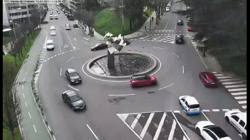 A traffic roundabout with several cars moving around it on a mostly clear day.