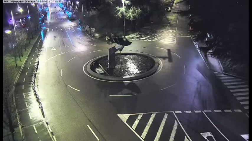 A nighttime overhead view shows a roundabout with a fountain in the center, surrounded by roadways and crosswalks.