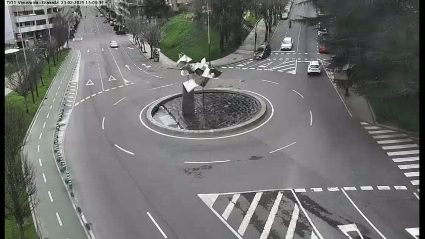 A roundabout with a modern sculpture in the center is surrounded by roads with sparse traffic on an overcast day.