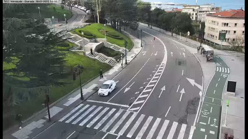 A curved road with a bike lane and crosswalks winds through a park-like area on a partly cloudy day.
