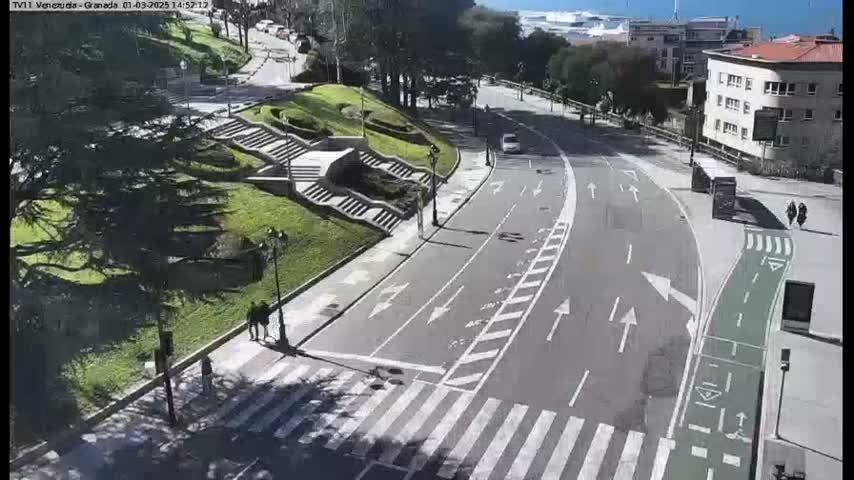 A sunny day overlooking a curved roadway with pedestrian crosswalks, bike lanes, and stairs leading to a grassy area with trees and buildings in the background.