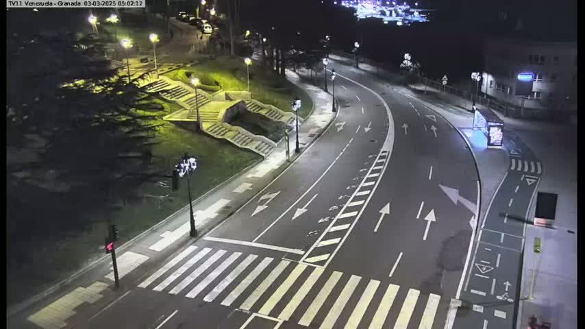 A nighttime, high-angle view shows a curving road with crosswalks and streetlights, alongside a landscaped area with stairs and trees.