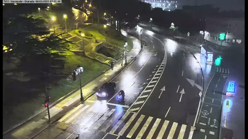 A rain-slicked road curves through a city at night, with a pedestrian crossing and a vehicle stopped near a crosswalk.