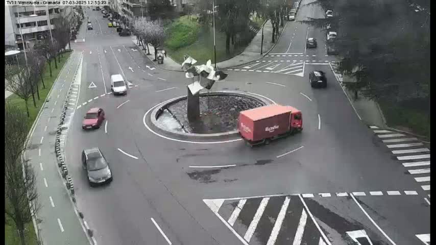 A roundabout with several cars and a delivery truck, under an overcast sky.