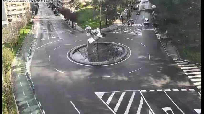 A circular roundabout with a modern sculpture in the center is surrounded by roads with a few cars, and bike lanes, all under a clear sky.