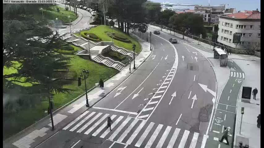 A curved road with a crosswalk and bike lane, flanked by green grassy areas and buildings, on an overcast day.