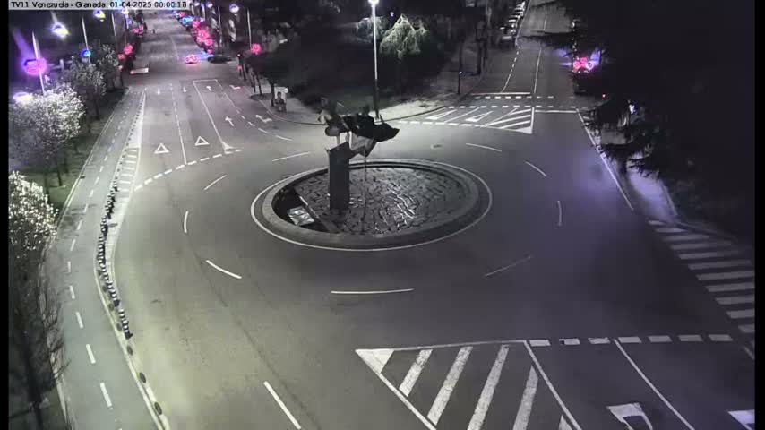 A nighttime aerial view of a roundabout with a sculpture in the center, surrounded by roads and pedestrian crossings.
