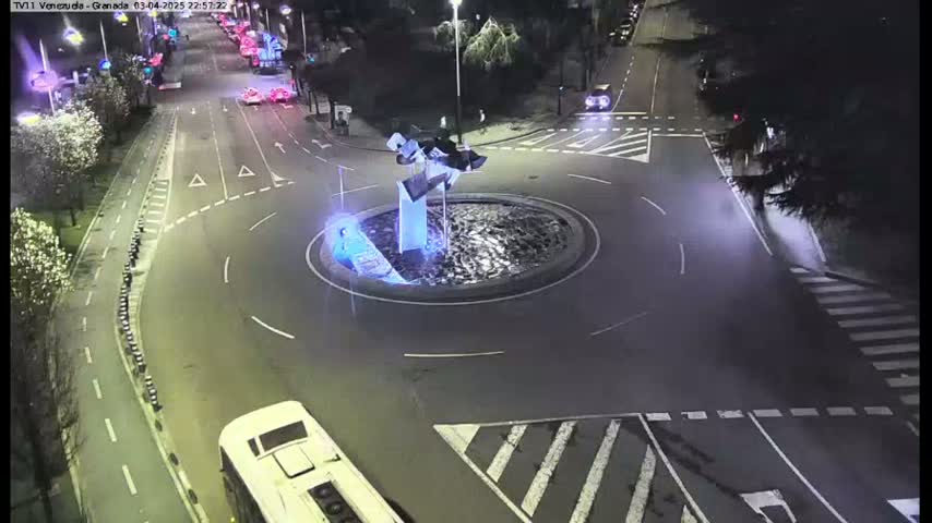 A nighttime overhead view shows a roundabout with a modern sculpture in the center, surrounded by roads and vehicles.