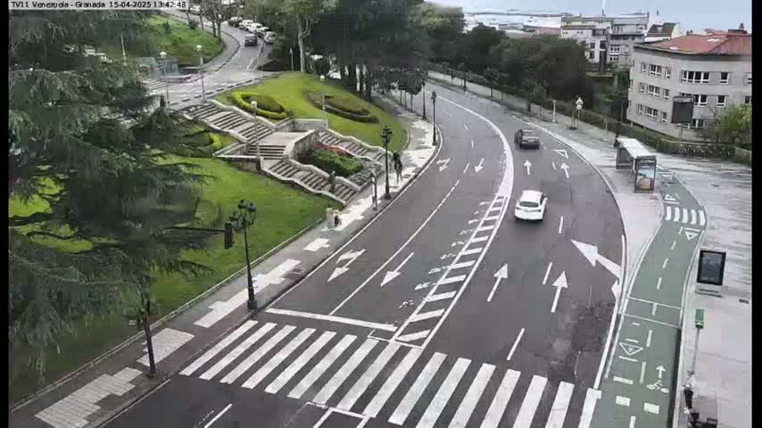 A curved road with a pedestrian crossing and a bike lane passes by a grassy area with stairs, under an overcast sky.