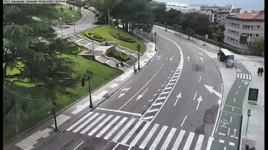 A mostly empty roadway curves through a landscaped area with stairs and trees under an overcast sky.