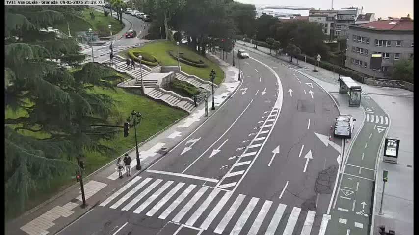 A curved road with a crosswalk and bike lane winds through a city park under a cloudy sky.