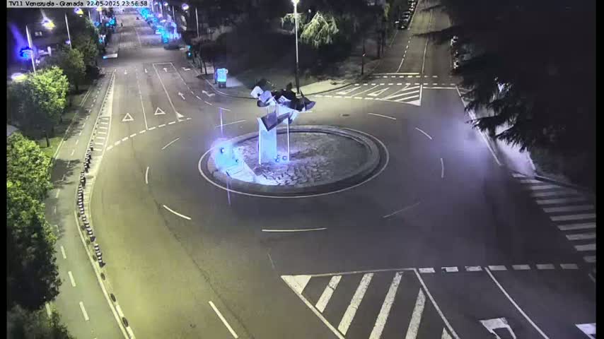 A nighttime overhead view shows a roundabout with a modern sculpture in the center, surrounded by roads with minimal traffic.