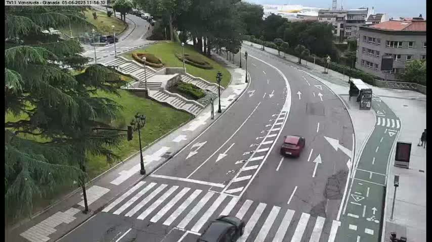 A curved road with a crosswalk and bike lane is seen from an elevated vantage point, under partly cloudy skies.