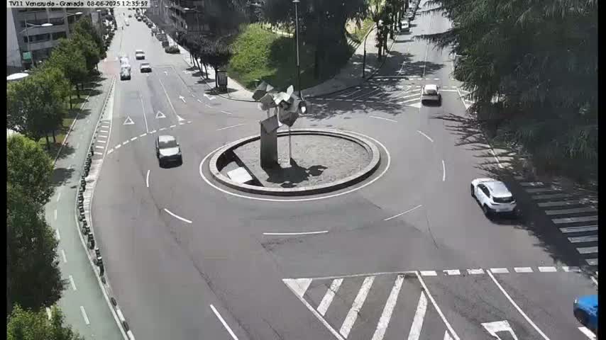 A traffic circle with several cars driving around it on a sunny day.