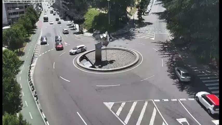 A sunny day shows several cars navigating a roundabout with a sculpture in the center, near a bike lane and crosswalk.