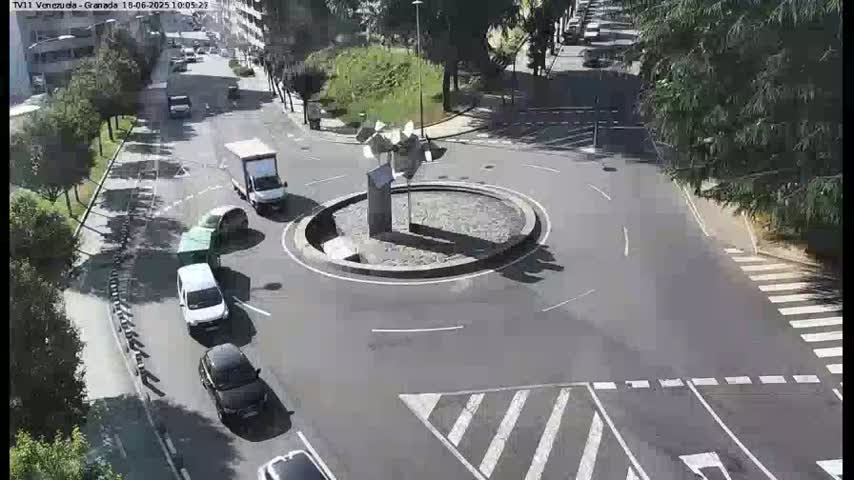 A sunny day shows several cars navigating a roundabout with a modern sculpture in the center.