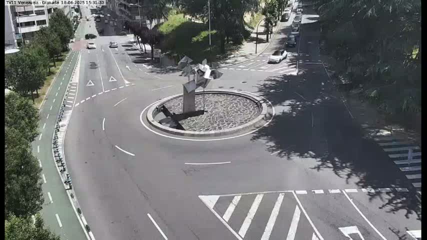 A roundabout with a modern sculpture in the center is surrounded by roads with cars and a bike path on a sunny day.