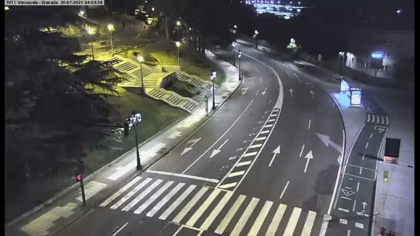Several cars are driving around a roundabout with a modern sculpture in the center, on a sunny day.