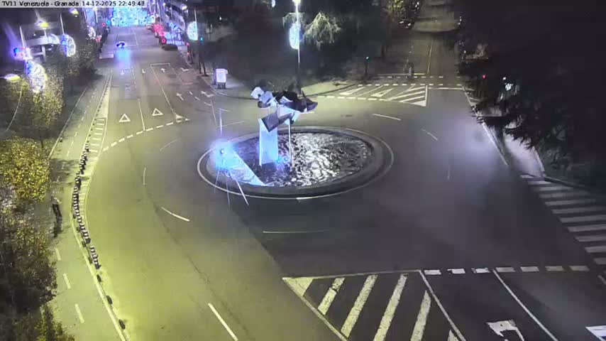 An aerial view captures a curved urban street featuring a multi-lane road, a dedicated green bike lane, and a crosswalk where a white car is stopped, with pedestrians on the sidewalks, lush green parkland with staircases to the left, and buildings leading to a harbor with ships in the distance on the right, all under an overcast sky.
