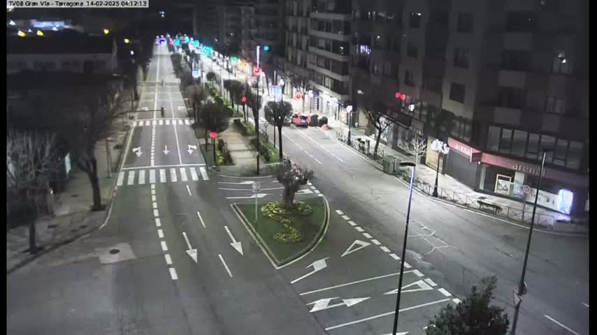 A nighttime, street-level view of a mostly empty city street with a few cars and pedestrians, illuminated by streetlights.