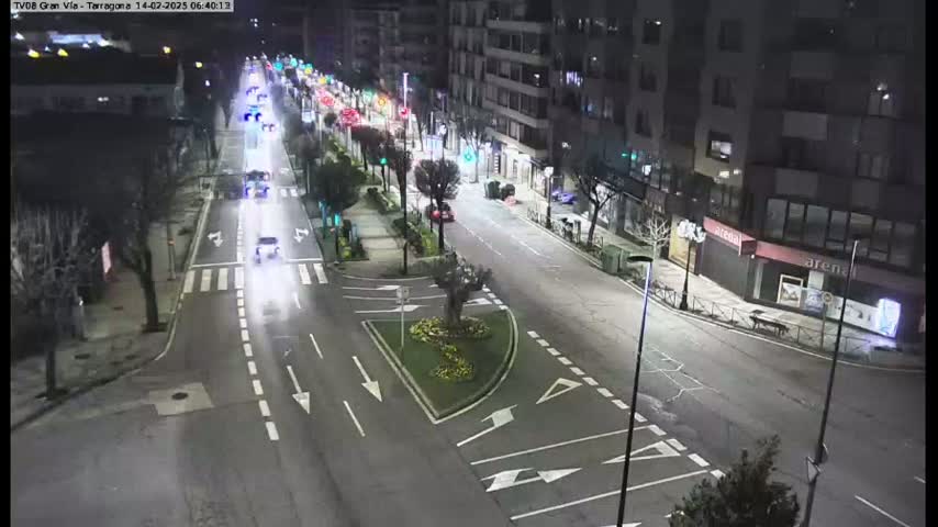 A nighttime, high-angle view of a city street with several cars driving on it, passing buildings with streetlights illuminating the scene.