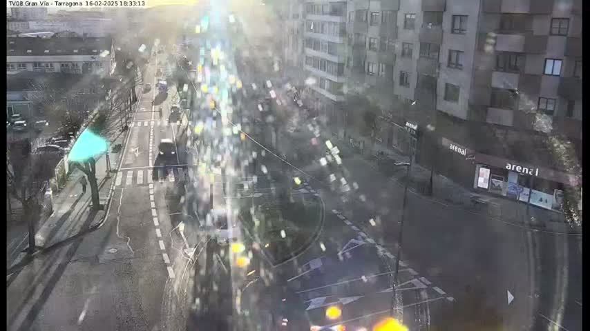 A sunny, slightly hazy day overlooks a city street intersection with several cars and buildings visible.