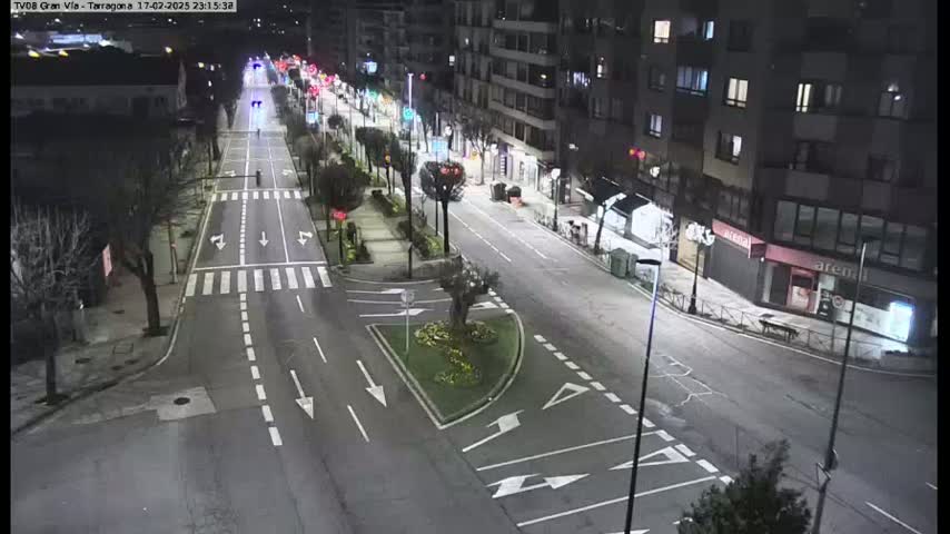 A nighttime, high-angle view of a mostly empty city street with minimal traffic, lined with buildings and streetlights.
