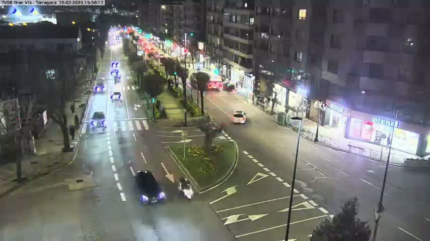 A nighttime, high-angle view of a city street with several cars driving on a multi-lane road, passing through a street intersection.