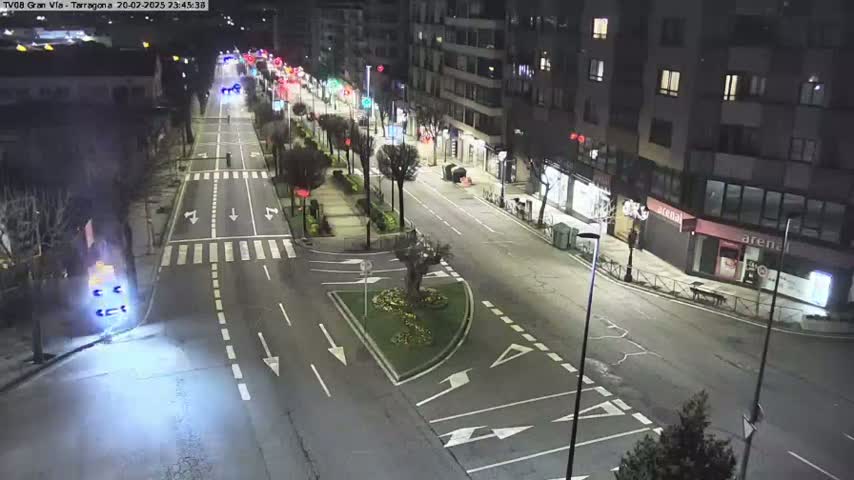 A mostly empty city street at night, lit by streetlights, with a few vehicles visible in the distance.