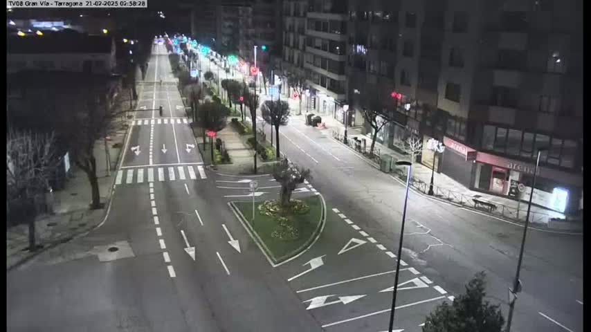 A mostly empty city street at night, illuminated by streetlights, with a few cars and pedestrians visible.
