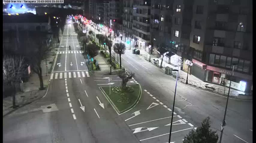 A nighttime view of a mostly empty city street with buildings lining both sides, illuminated by streetlights.